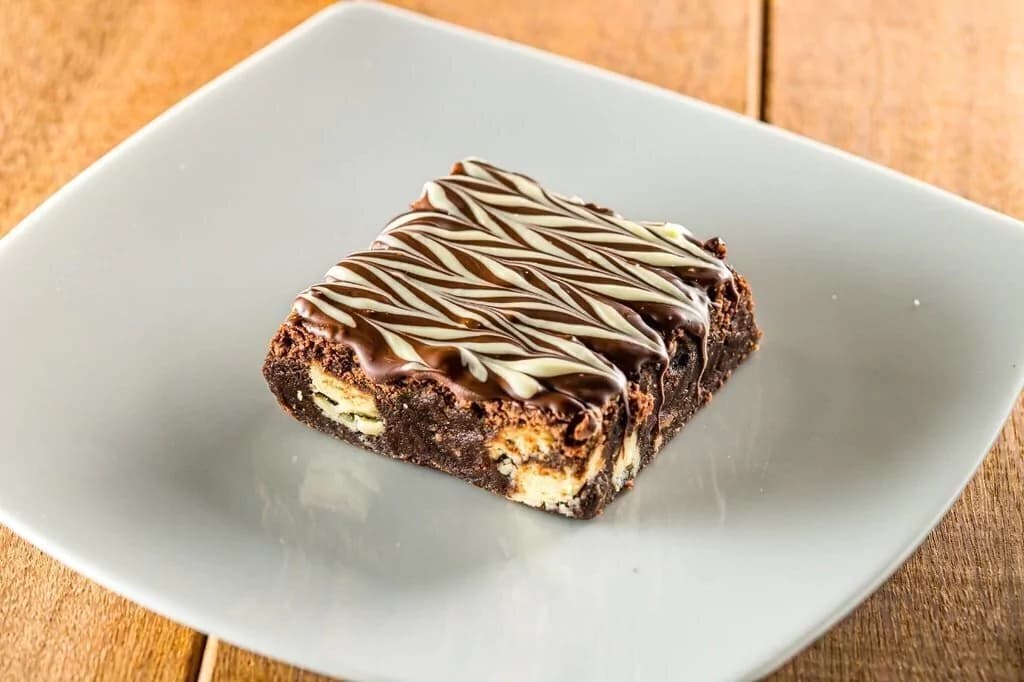 Brownie Três Chocolates com cobertura de chocolate, servido em prato branco